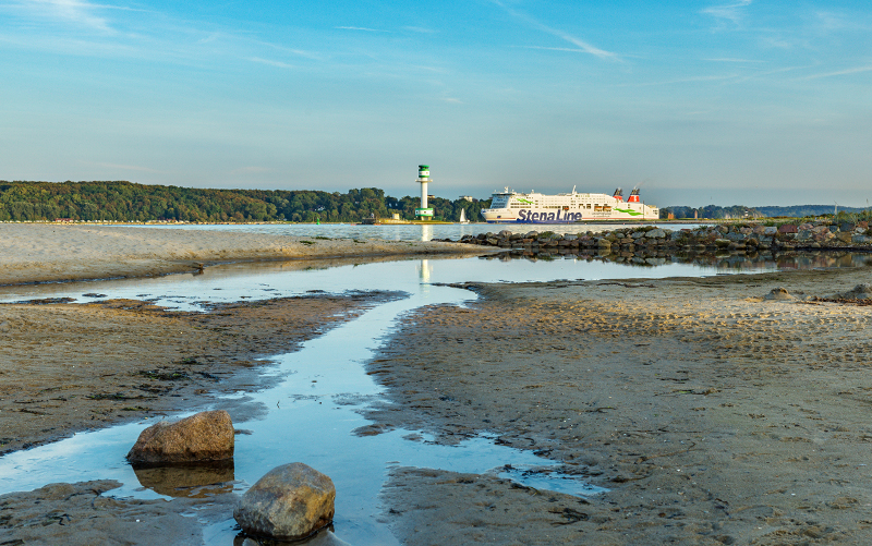 Blick vom Strand auf eine Fähre und den Kieler Leuchtturm