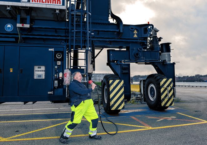 Mitarbeiter*in des PORT OF KIEL mit Kabel in der Hand vor einem Kran