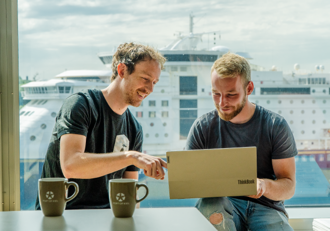 Mitarbeitende der IT Abteilung arbeiten am Laptop. Im Hintergrund ist die Color Line Fähre zu sehen.