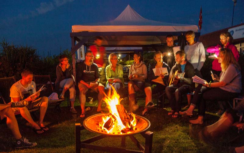 Gruppenbild Mitarbeitende sitzen um Lagerfeuer