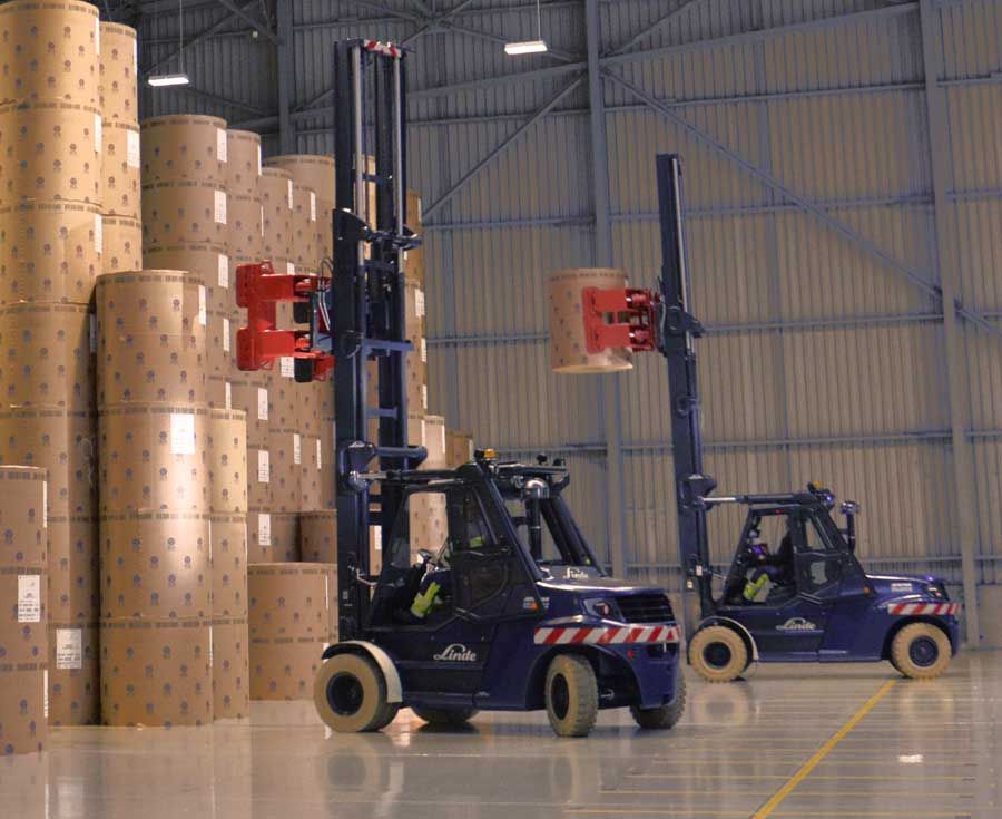 Two forklifts handle rolls of paper in the paper hall.